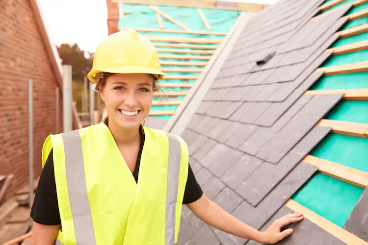 roofers-insurance-female Female roofer standing on a roof smiling