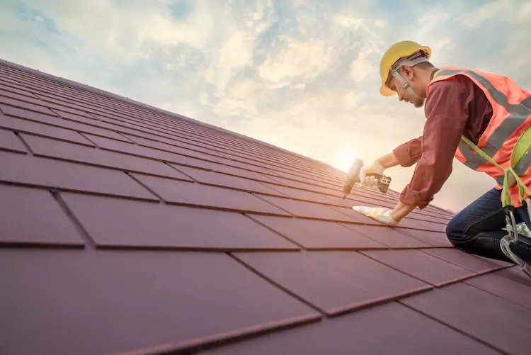 roofers-insurance-sunset Insured roofer on a roof drilling in a tile at sunset