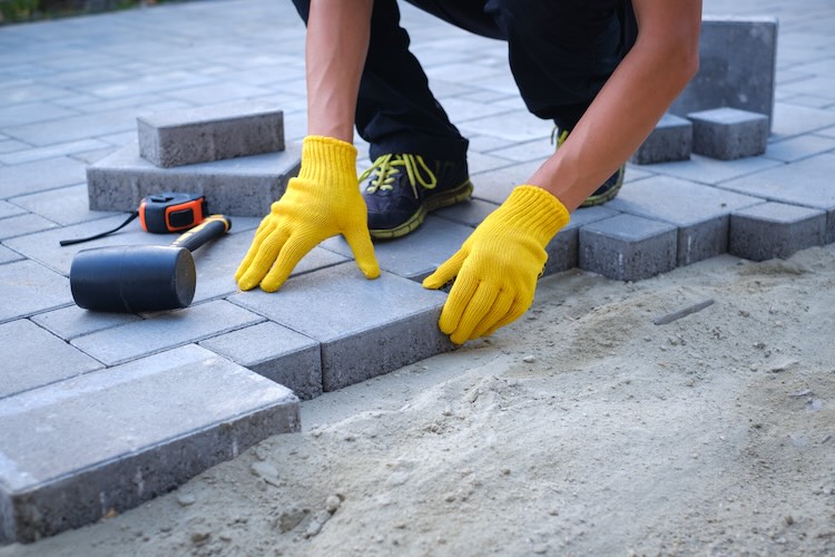 The master in yellow gloves lays paving stones Garden brick pathway paving by professional paving contractor
