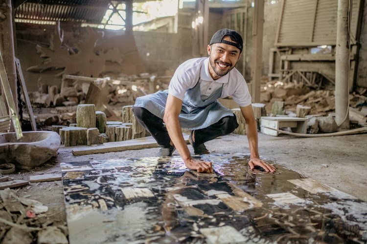 Smiling stonemason squats while washing large squares of stone Smiling stonemason squats while washing large squares of stone in the workshop